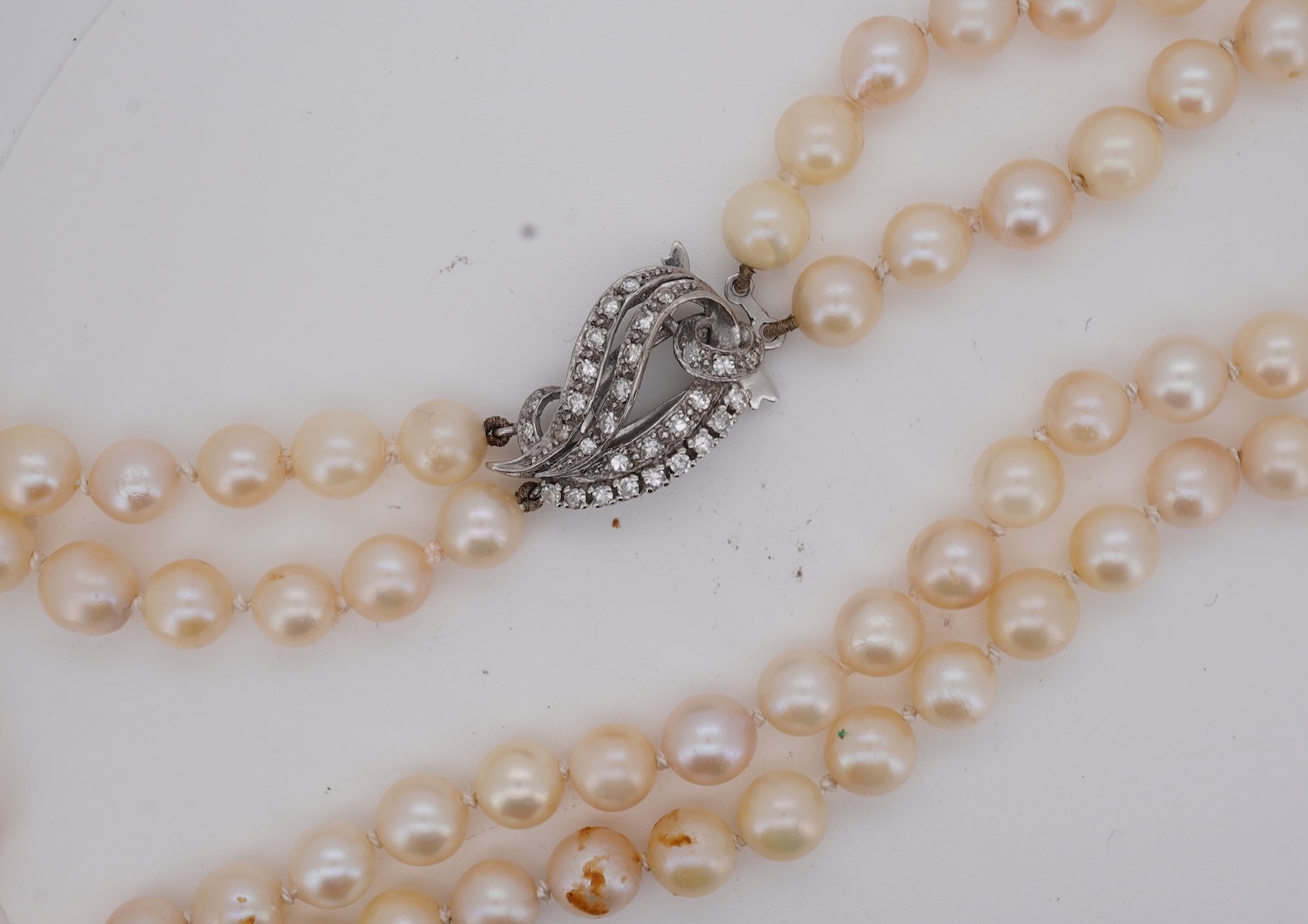 A twin strand cultured pearl necklace with a diamond cluster set white metal scroll shaped clasp, 60cm.